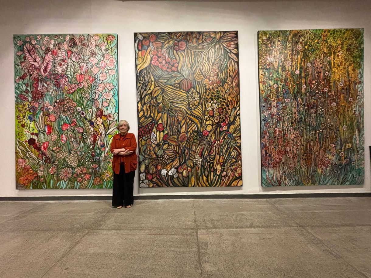 Tânia Carneiro Leão diante de dois de seus grandiosos painéis coloridos